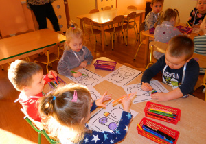 Dzieci przy stolikach kolorują kontur misia