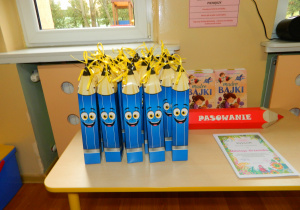 Widok prezentów na pasowanie: papierowe duże ołówki, książki oraz dyplomy dla dzieci