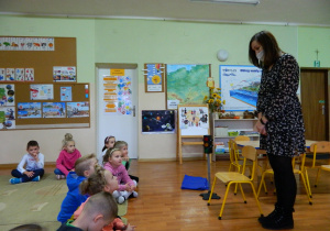 Dzieci siedzą na dywanie, przed nimi stoi pani Małgosia i opowiada o pracy policji