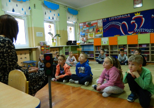 Dzieci siedzą na dywanie słuchając prelekcji pani policjantki
