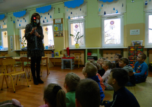 Dzieci siedzą na dywanie, przed nimi pani Małgosia prezentuje miniaturkę sygnalizatora świetlnego