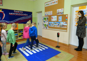 Dzieci przechodzą przez atrapę pasów położonych na dywanie