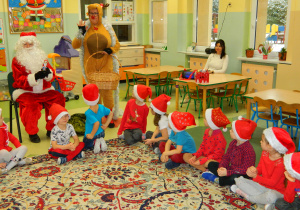 Renfer Rudolf wraz z mikołajem czestują dzieci czekoladowymi Mikołajami