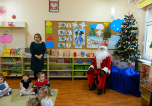 Mikołaj siedzi przed choinką a pani dyrektor składa życzenia świateczne w grupie Wiewiórek