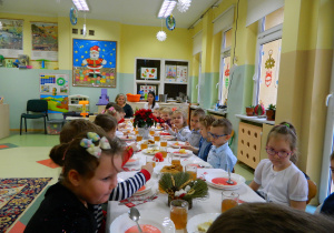 Dzieci z grupy Misiów siedzą przy wspólnym stole wigilijnym nakrytym białym obrusem i spożywają obiad