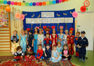 Dzieci z grupy Biedronek w przebraniach pozuja do wspólnej fotografi na tle napisu Bal karnawalowy