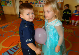 Dziewczynka i chłopiec trzymają balon swoimi brzuchami aby nie wypadł podczas tańca
