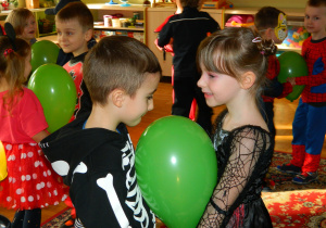 Chłopiec z dziewczynką trzymają zielony balon pomiędzy brzuchami aby nie wypadł podczas tańca