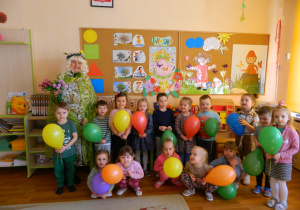Zdjęcie grupowe Wiewiórek , dzieci na tle dekoracji z pania Lucynką trzymają w rękach kolorowe balony.