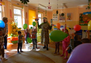 Dzieci trzymają kolorowe balony i w kole bawią się z panią Lucynką.