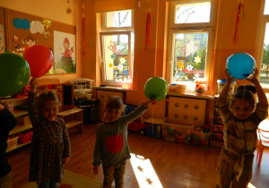 Dziewczynki unoszą ręce trzymając balony.