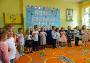 Dzieci z grupy Krasnali stoja w półkolu i śpiewają dla rodziców.