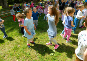 Dzieci wspólnie tanczą w ogrodzie przedszkolnym do muzyki.
