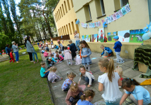 Dzieci maluja kredą po chodniku.