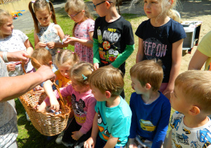 Dzieci częstuja się cukierkami z wiklinowego koszyka.
