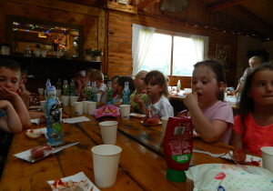 Przedszkolaki jedzą wspólnie kiełbaski z grilla.
