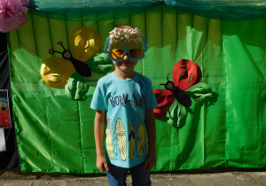Chłopiec w ozdobionych okularach popcornem stoi na tle zielonej dekoracji w motyle.