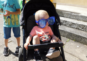 Chłopiec siedzi w wózku z ogromnymi niebieski okularami na nosie.