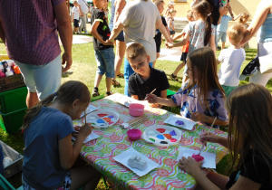 Dzieci siedza przy stoliku i ozdabiają farbami gipsowe kształty.