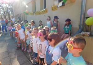 Dzieci stoja w rzędzie w ozdobionych okularach czekając na wyniki konkursu.