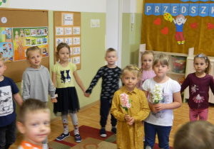 Dziewczynki stoją w środku koła trzymając kwiaty z bibuły podczas wspolnej zabawy.