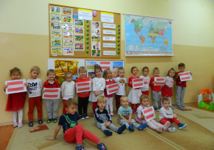 Dzieci z grupy Krasnali trzymaja w rękach flage Austrii, stoją i siedzą na tle dekoracji.