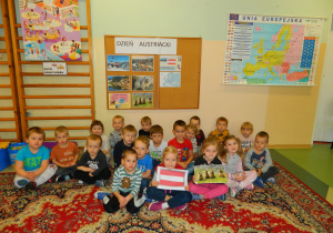 Dzieci z grupy Biedronek siedza na dywanie z flagą Austrii i zdjęciem świstaka na tle dekoracji.
