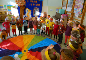 Dziewczynki i chłopcy stoją wokół dużej chusty w kolorach tęczy