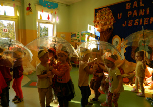 Przedszkolaki chowają się pod parasolami podczas zabawy