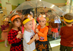 Przedszkolaki chowają się pod parasolami podczas zabawy