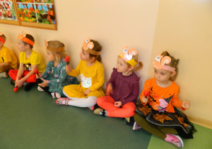 Przedszkolaki grają na instrumentach muzycznych siedząc pod ścianą