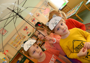 Przedszkolaki chowają się pod parasolem w trakcie zabawy