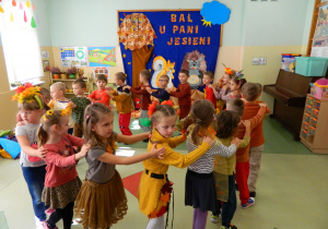 Dzieci tańczą w kole trzymając się za ramiona w przebraniach jesiennych