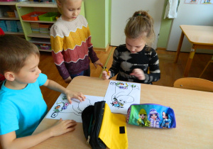 Dzieci siedzą przy stoliku i kolorują postać muminka