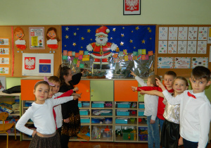 Starszaki stoją w dwoch rzędach wskazując palcem na ilustracje Mikołaja