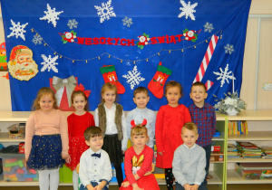 Przedszkolaki stoją i siedzą przy świątecznej dekoracji