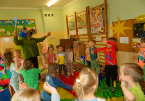 Pani Lucynka w przebraniu wiosny tańczy z dziećmi w kole unoszącymi ręce do góry