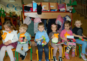 Przedszkolaki siedzą na krzesełkach trzymając w rękach nagrody
