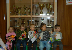 Przedszkolaki siedzą na krzesełkach trzymając w rękach nagrody