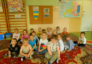 dzieic z grupy Biedronki siedza na dywanie przy tablicy z napisem Dzień Ukraiński, flagą, zdjęciami tego kraju