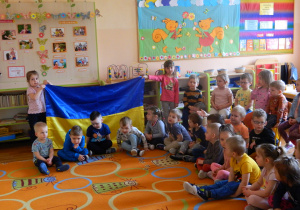 Przedszkolaki z najmłodszych grup oglądaja dużą flagę ukraińską trzymaną przez Alisę i Anhelinę