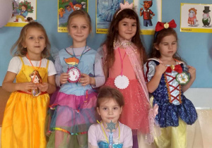 Dziewczynki w przebraniach księżniczek stoją na tle dekoracji.