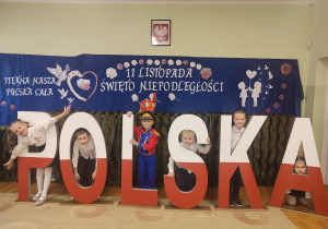 Dzieci stoją przy dużych literach z napisem Polska