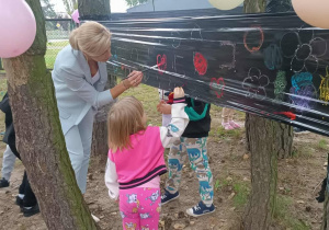 Pani dyrektor wraz z Dorotką maluje farbami na czarnej foli