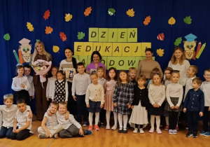 Dzieci wraz z nauczycielami i dyrektorem stoją na tle derkoracji