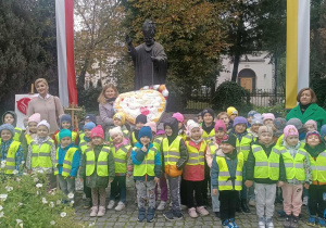 Dzieci wraz z nauczycielami i panią dyrektor stoją przy pomniku Jana Pawła II