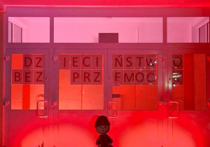Wejście do przedszkola podświetlone na czerwono z napisem Dzieciństwo bez przemocy