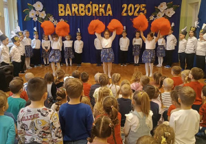 Dziewczynki tańczą z pomarańczowymi pomponami.