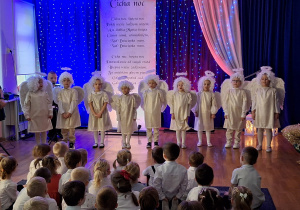 Dzieci w przebraniach aniołków śpiewają kolędy.