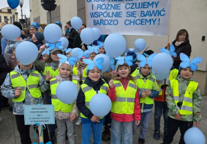 Dzieci trzymają w dłoniach niebieskie balony idąc w pochodzie z okazji Dnia Autyzmu.